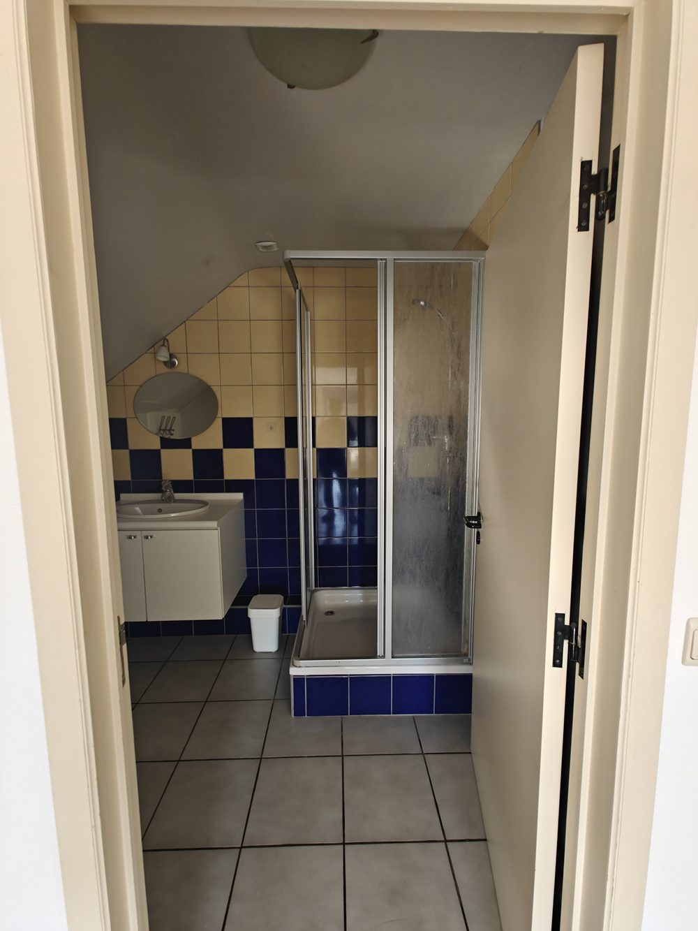 Avant travaux : salle de bain carrelée en damier bleu et jaune avec ancienne cabine de douche