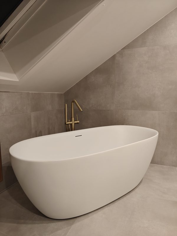 Baignoire îlot blanche et robinetterie sur pied dans une salle de bain en béton ciré